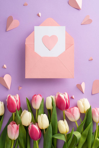 Muttertagsgeschenk. Top vertikale Ansicht flache Lage von hübschen rosa Papierherzen und Tulpenblumen mit Umschlag mit Grußkarte auf weichem violettem Hintergrund - Foto, Bild