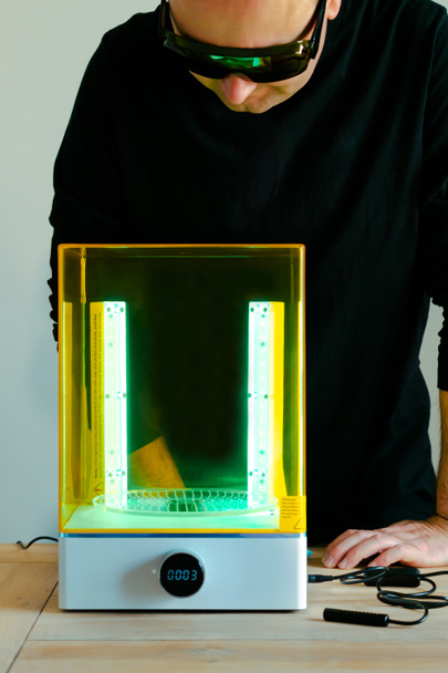 Muž nosí brýle, upravuje pračku a vytvrzuje pomocí UV světla před použitím, pro 3D pryskyřičnou tiskárnu - Fotografie, Obrázek