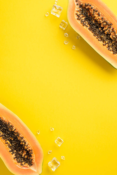 Koncepcja tropikalnej oazy. Góra widok pionowy świeżych plasterków papai z kostkami lodu na żółtym tle z pustym miejscem na reklamę. - Zdjęcie, obraz