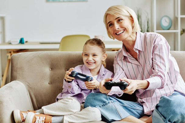 Sarışın genç bir kadının portresi. Küçük bir kızla video oyunu oynayıp evde birlikte eğleniyor. - Fotoğraf, Görsel