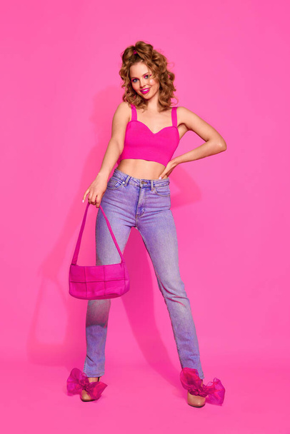 Portrét krásné dívky žena na sobě stylové oblečení, džíny a top pózování přes růžové studio pozadí. Glam fashionista. Pojem móda, krása, retro, mládež, životní styl, reklama - Fotografie, Obrázek