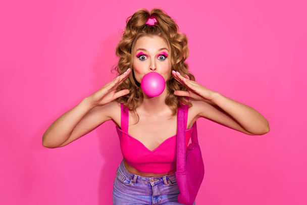 Mädchen mit Blasengummi. Porträt der schönen Frau trägt stilvolle Kleidung, Jeans und Top posiert über rosa Studiohintergrund. Konzept der Mode, Schönheit, Jahrgang, Jugend, Lebensstil, Anzeige - Foto, Bild