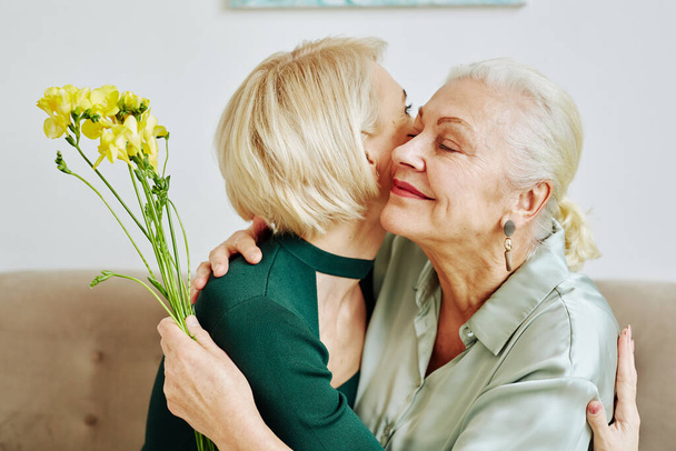 Side view portrait of adult daughter embracing mother and giving her flowers on Mothers day - 写真・画像