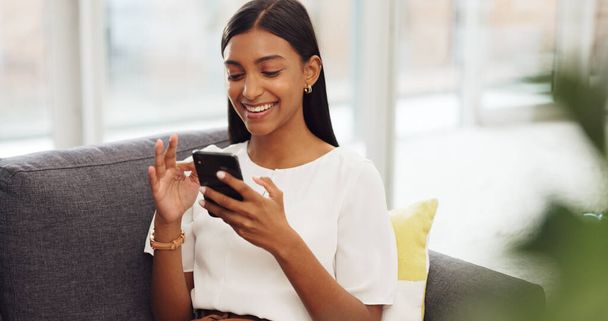 Happy girl with phone relax on sofa or living room couch while laughing or smile at a meme. Young girl with mobile at home, house or apartment doing a internet or web search for funny comedy videos. - Foto, imagen