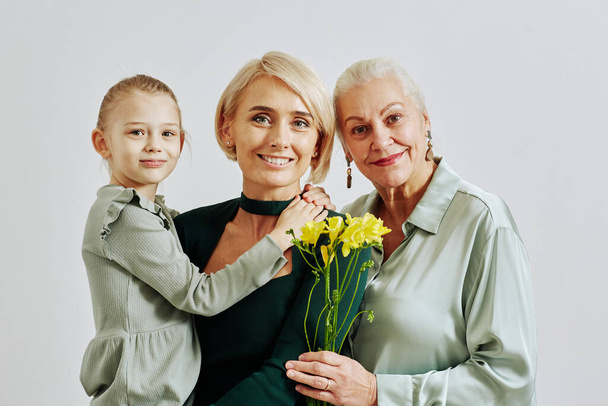 Minimal portrait of three women in family holding flowers and smiling at camera in studio - Photo, Image