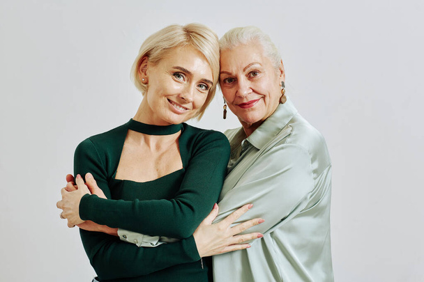 Minimal waist up portrait of smiling senior woman with adult daughter both looking at camera in studio - Photo, image