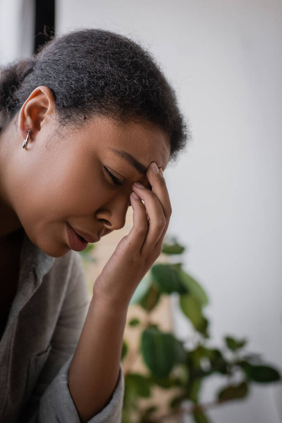 Депресивна багаторасова жінка плаче і торкається лоба вдома
  - Фото, зображення