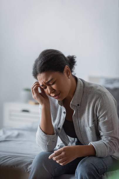 displeased multiracial woman sitting with closed eyes while having migraine  - Foto, Bild