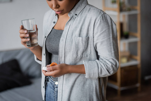 Cropped view of multiracial woman holding antidepressant pills and water at home  - Fotoğraf, Görsel