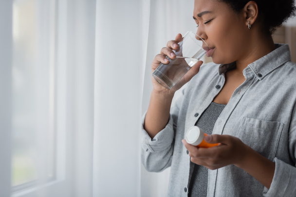 multiracial woman with depression taking pill and drinking water at home  - Foto, Imagem