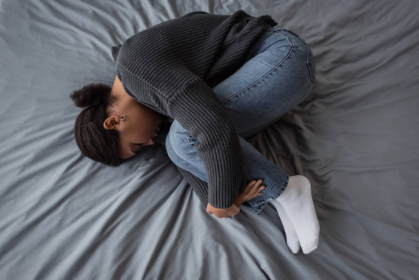 Widok z góry na wielorasową kobietę z problemami psychicznymi leżącą na łóżku w domu  - Zdjęcie, obraz