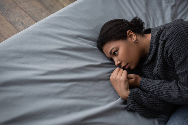 Κάτοψη της πολυφυλετικής γυναίκας με κατάθλιψη κοιτάζοντας αλλού, ενώ βρίσκεται στο κρεβάτι - Φωτογραφία, εικόνα