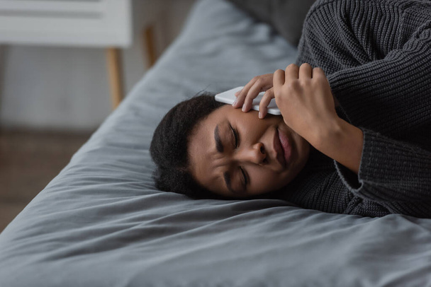 Femme multiraciale déprimée appelant le service d'assistance téléphonique alors qu'elle était allongée sur son lit à la maison  - Photo, image