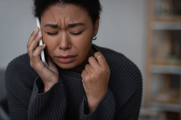 Crying multiracial woman talking on smartphone with helpline at home  - Foto, Imagem