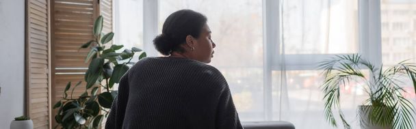 Vista laterale della donna multirazziale frustrato in maglione guardando lontano a casa, banner  - Foto, immagini