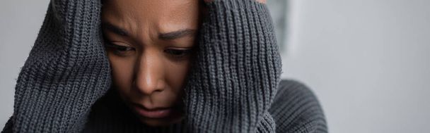 Worried multiracial woman in sweater touching head at home, banner  - Photo, Image
