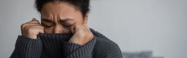 Deprimida mujer multirracial en suéter de punto llorando en casa, pancarta  - Foto, Imagen
