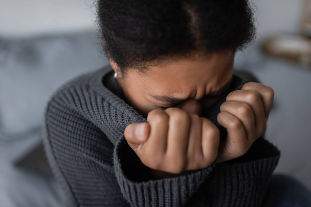 Mulher multirracial triste em suéter chorando no quarto embaçado em casa  - Foto, Imagem