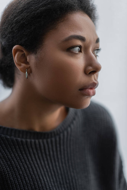 Frustrated multiracial woman in grey knitted sweater looking away at home  - Foto, afbeelding