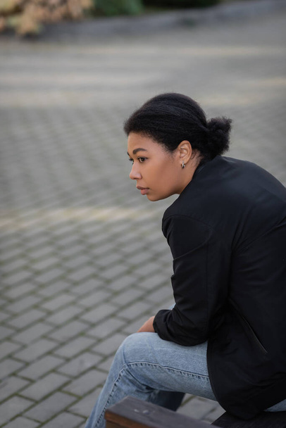 Νεαρή πολυφυλετική γυναίκα με διανοητικό πρόβλημα κάθεται στον πάγκο σε εξωτερικούς χώρους  - Φωτογραφία, εικόνα
