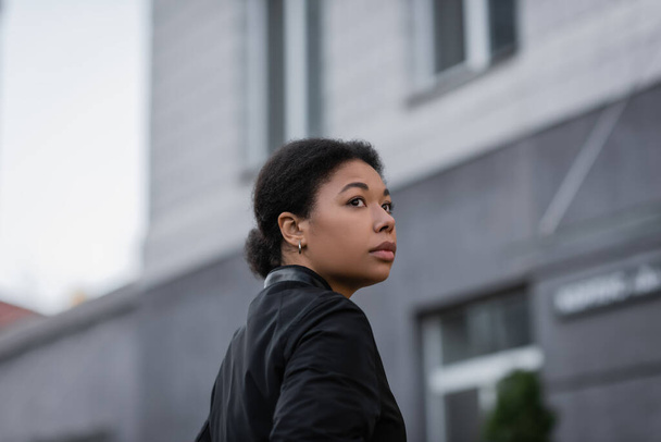 Frustrated multiracial woman in jacket standing on blurred urban street  - Fotó, kép