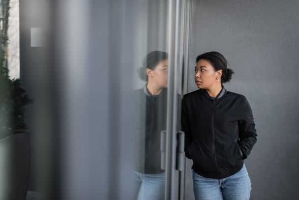 wielorasowa kobieta z depresją patrząc na szkło na drzwiach budynku na zewnątrz  - Zdjęcie, obraz