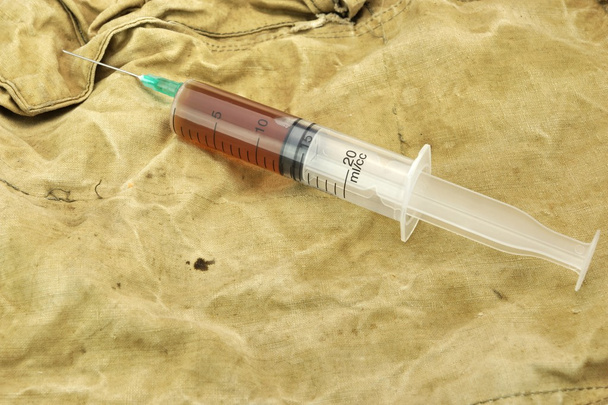 Jeringa médica con líquido marrón en el bolso del ejército del camuflaje
 - Foto, imagen