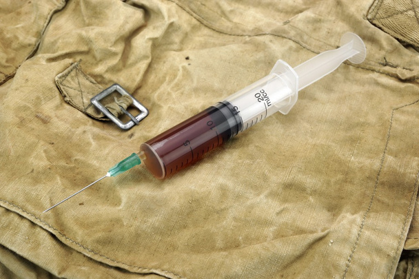 Medizinische Spritze mit brauner Flüssigkeit auf Tarntasche - Foto, Bild