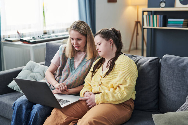 Jovem com síndrome de Down e sua irmã passando tempo juntos em casa sentados no sofá assistindo filme na Internet no laptop - Foto, Imagem