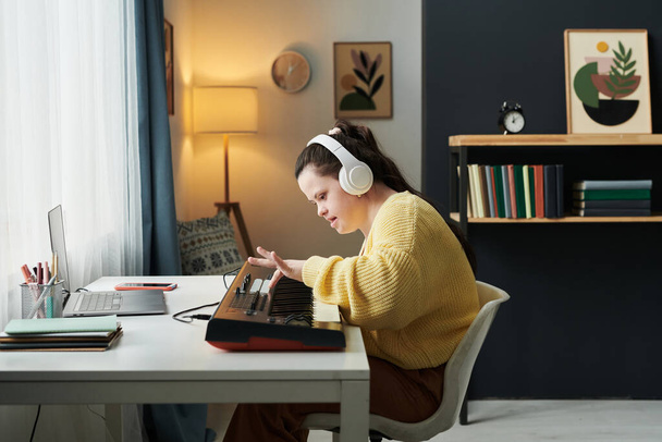Side view of young Caucasian woman with down syndrome wearing headphones learning to play electronic keyboard - Foto, immagini
