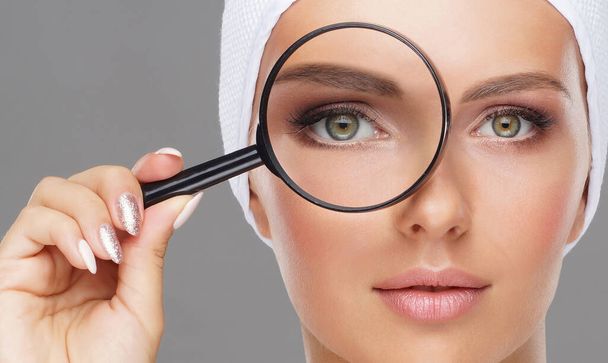 Face of young and beautiful girl and a magnifying glass. Plastic surgery, face lifting and aesthetic medicine concept. - Photo, image