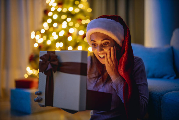 Улыбающаяся женщина дома открыла подарочную коробку, сюрприз! Счастливого Рождества!. - Фото, изображение
