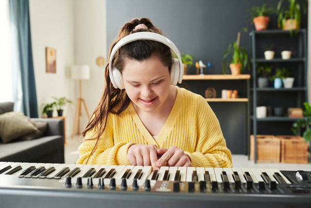 Портрет радісної молодої кавказької дівчини з синдромом Дауна, одягненої в навушники, проводить час вдома, навчаючись грати на електронній клавіатурі. - Фото, зображення