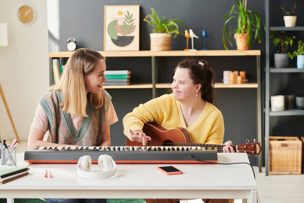 Nuori valkoihoinen nainen istuu vieressä hänen naispuolinen opiskelija Downin oireyhtymä opettaa häntä soittamaan kitaraa - Valokuva, kuva