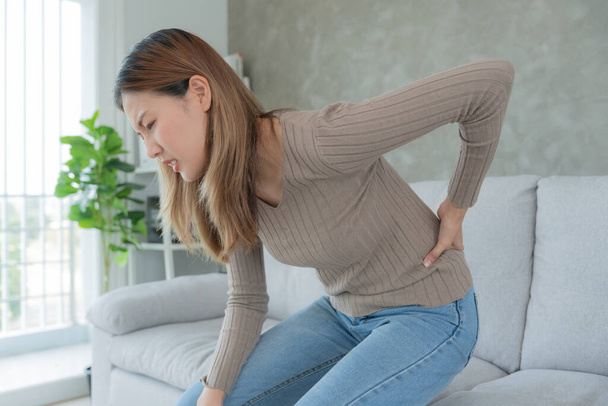 Asia beautiful woman holding her lower back while and suffering from unbearable pain health and problems, chronic back pain, backache in office syndrome, scoliosis, herniated disc, muscle inflammation - Фото, зображення