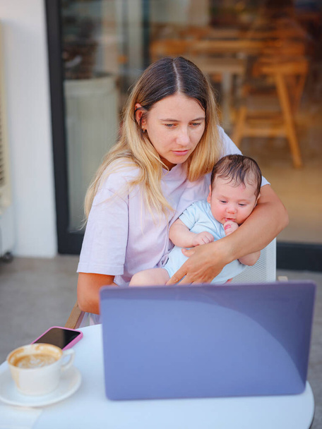 Diverse people portrait. Creative businesswoman balancing work and motherhood. Beautiful young mother working with laptop computer and breastfeeding, holding and nursing her newborn baby at cafe. - Photo, Image