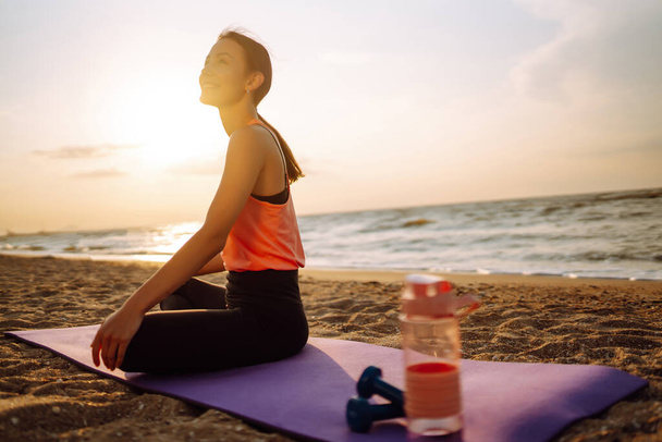 Modern young woman doing yoga on the beach at sunrise. Sports woman doing stretching outdoors. The concept of an active lifestyle, sports training, yoga or fitness. - Valokuva, kuva