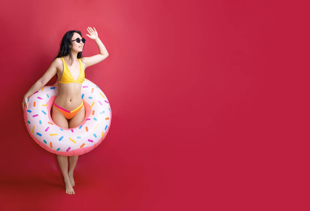 Full length happy young sexy asian woman slim body wear swimsuit posing with inflatable rubber ring isolated on pink color wall background studio. Summer hotel pool sea rest sun tan concept - Fotoğraf, Görsel