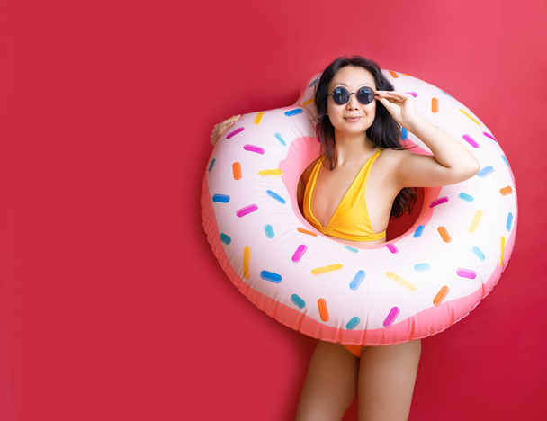 Happy fun young sexy asian woman slim body wear swimsuit hold pink inflatable ring isolated on vivid red color wall background studio Summer hotel pool sea rest sun tan concept - Photo, Image