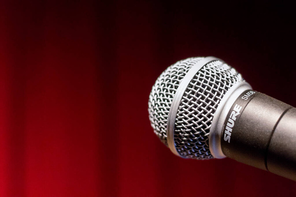 крупный план кривого микрофона на фоне красного занавеса сцены - Фото, изображение