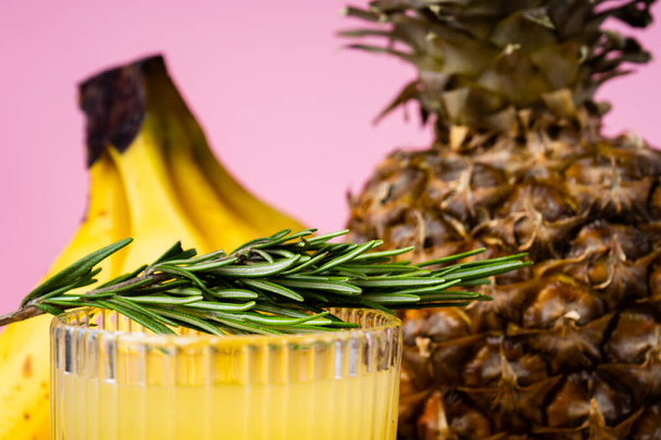 zijaanzicht van een glas ananassap en een ananas op felroze achtergrond - Foto, afbeelding