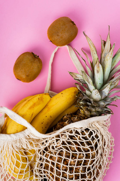 bananas, kiwi and pineapple in a beige string bag on pink background - Photo, Image