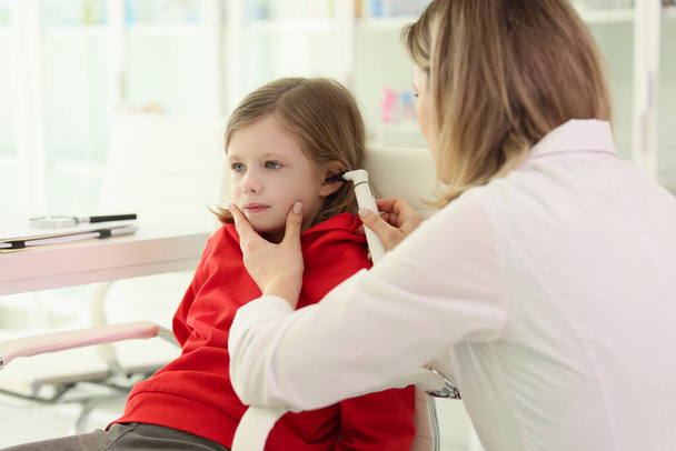 Le médecin soignant vérifie les oreilles de la petite fille avec du matériel médical dans le bureau de la clinique. L'enfant fait un contrôle régulier en prenant soin de son état de santé - Photo, image
