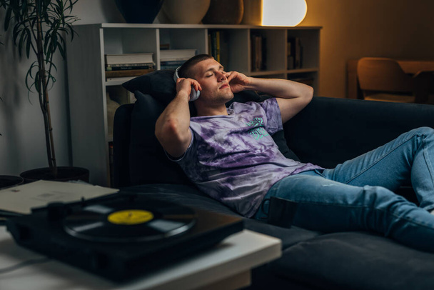 A Caucasian man puts on headphones to listen to records and relax at night - Foto, imagen