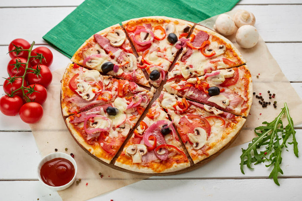 Taze pişmiş sosis, kırmızı biber, mantar, soğan ve zeytinli pizza ahşap zemin üzerinde domates, sos ve bitkilerle servis edilir. Yemek teslimatı konsepti. Restoran menüsü - Fotoğraf, Görsel