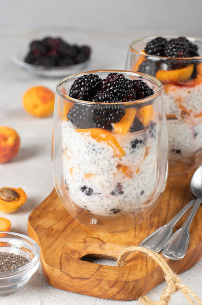 Chia pudding with blackberries and apricots in two glass on wooden board on gray background, Vertical format - Foto, Imagem