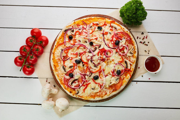 Freshly baked Vegetarian pizza with Tomatoes, mushrooms, red pepper, olives, onion and Mozzarella served on wooden background with sauces and herbs. Food delivery concept. Restaurant menu - Photo, image