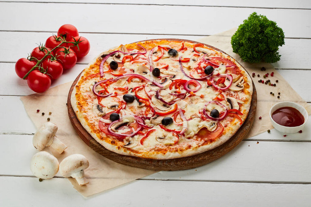Pizza végétarienne fraîchement cuite avec tomates, champignons, poivron rouge, olives, oignon et mozzarella servie sur fond de bois avec des sauces et des herbes. Concept de livraison de nourriture. Menu restaurant - Photo, image