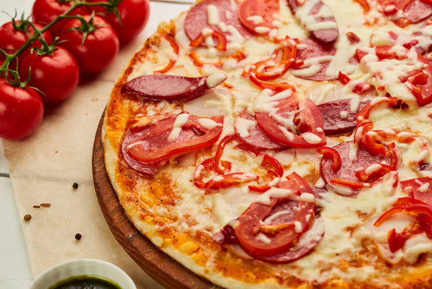 Świeżo upieczona pizza z wędzonymi kiełbaskami, czerwoną papryką i pomidorami serwowana na drewnianym tle z sosem i ziołami. Koncepcja dostarczania żywności. Menu restauracji - Zdjęcie, obraz