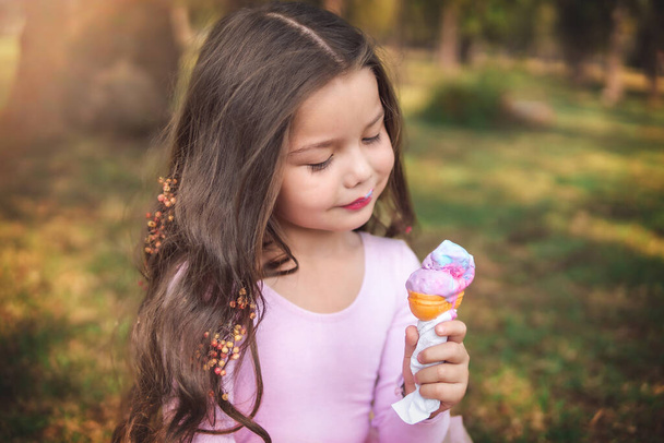 Cute blonde curly haired girl eating a nice ice cream in the forest on a nice summer day, children's day concept, happy girl enjoying a hot day. - Photo, Image